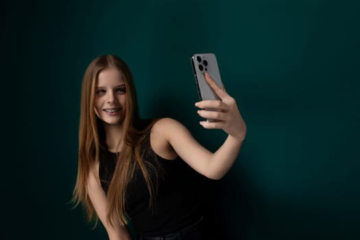 A woman is seen holding a cell phone at arms length, smiling and posing for a selfie. She is capturing the moment on her device to share with others on social media.