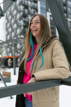 A woman wearing a pink shirt and tan jacket, standing confidently outdoors. She appears stylish and fashion-forward in her casual yet chic ensemble.