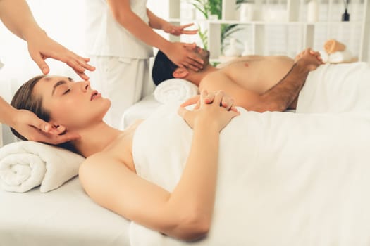 Caucasian couple enjoying relaxing anti-stress head massage and pampering facial beauty skin recreation leisure in dayspa modern light ambient at luxury resort or hotel spa salon. Quiescent