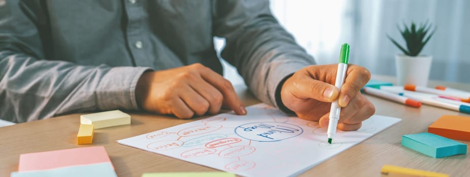 Skilled businessman brainstorms marketing ideas using mind maps. Successful male startup leader drafts financial plan on table with sticky notes scatter around. Closeup. Focus on hand.Variegated.