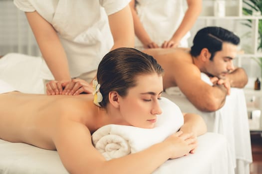 Caucasian couple customer enjoying relaxing anti-stress spa massage and pampering with beauty skin recreation leisure in day light ambient salon spa at luxury resort or hotel. Quiescent