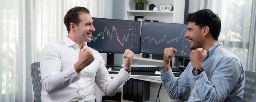 Cheerful two stock exchange traders raising fist up for digital achievement with panorama view on dynamic market data background. Successful investors earning high profit analyzed by graph. Sellable.