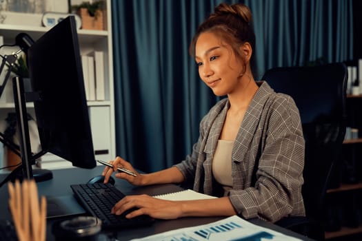 Beautiful businesswoman working on laptop for marketing plan on social media online, searching data report at over late night time at modern home office, working startup company project job. Infobahn.