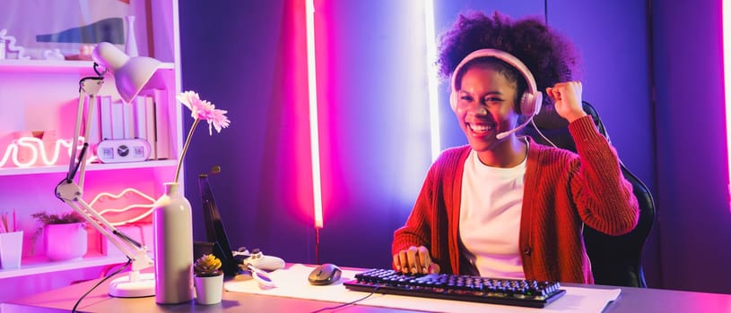 African American girl streamer playing online fighting with Esport skilled team wearing headphones in neon color lighting room. Talking other players planing strategies to win competitors. Tastemaker.