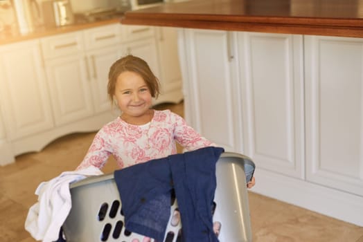 Smile, basket and child with laundry in home for learning to clean with development and growth. Happy, kitchen and portrait of girl kid with clothes for washing with housekeeping at apartment