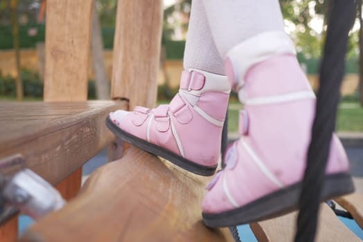 A little girl in orthosis shoes crosses a wooden bridge Child cerebral palsy disability..
