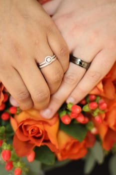 Couple Hands Wedding on Bouquet of Orange Roses