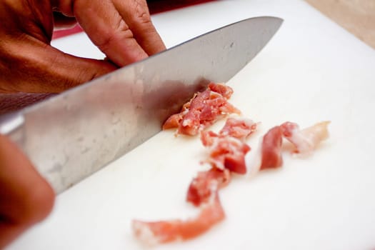 slicing up proscuitto with a knife to used as a topping