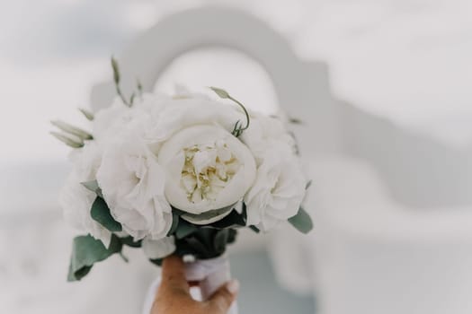 A bouquet of white flowers with green leaves is being held by a person's hand. The arrangement is simple and elegant, with the white flowers providing a clean and fresh look