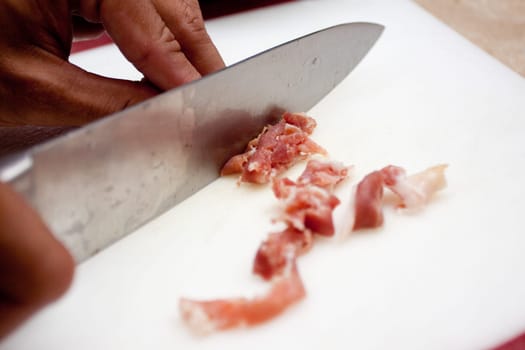 slicing up procuitto with a knife to used as a topping