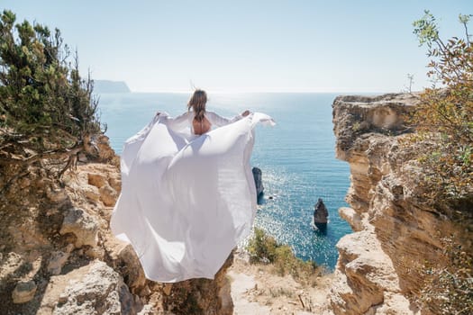 A woman in a white dress is standing on a rocky beach with her hat on. The scene is serene and peaceful, with the woman enjoying the view of the water.