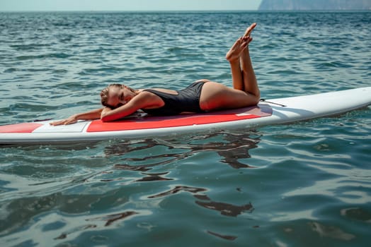 Woman sap sea. Sports girl on a surfboard in the sea on a sunny summer day. In a black bathing suit, he lies on a sap in the sea. Rest on the sea
