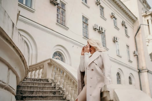 A woman in a white coat stands on a white staircase in front of a building. She is smiling and she is enjoying herself