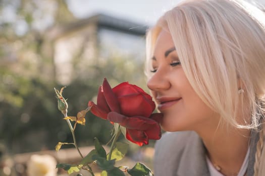 A woman is smelling a red rose. Concept of happiness and contentment, as the woman is enjoying the scent of the flower