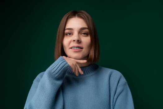 A woman wearing a blue sweater is striking a pose for a photograph. She looks directly at the camera with a confident expression, standing in a casual stance.