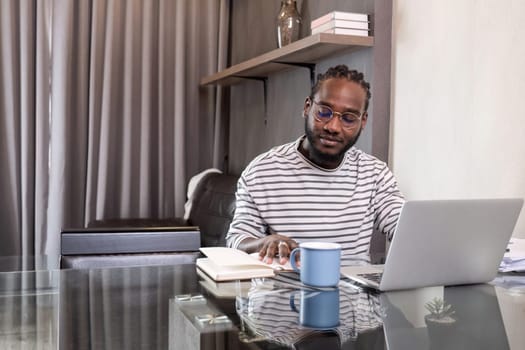 Young African American businessman spends his free time working from home on his laptop..