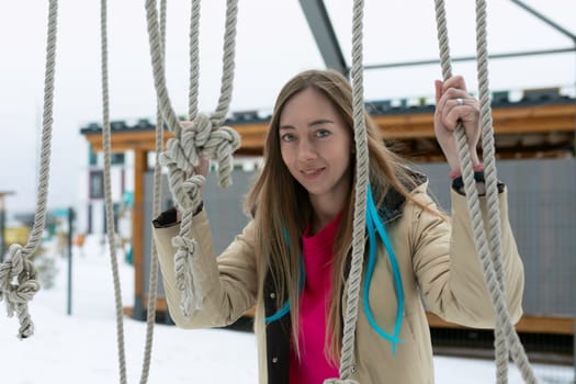 A woman is balancing on a rope stretched across a snowy landscape. She is steady and focused, with snow-covered trees in the background.