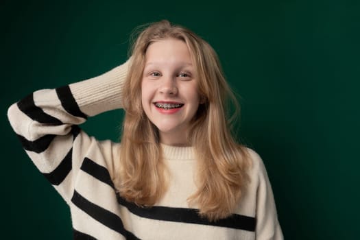 A woman with blonde hair is standing, wearing a striped sweater. She appears calm and is looking ahead. Her outfit consists of a striped sweater that complements her hair color.