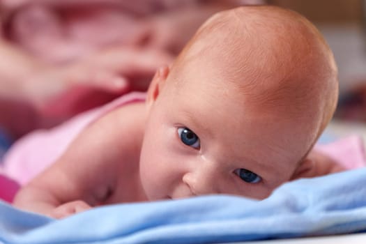 Newborn baby, at the tender age of two months, lies comfortably while curiously looking at the world around with bright, expressive eyes.