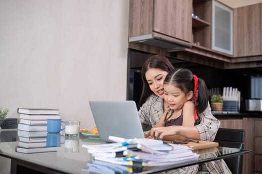 a single mother, sits at home working on a laptop with her daughter beside her watching and encouraging her..