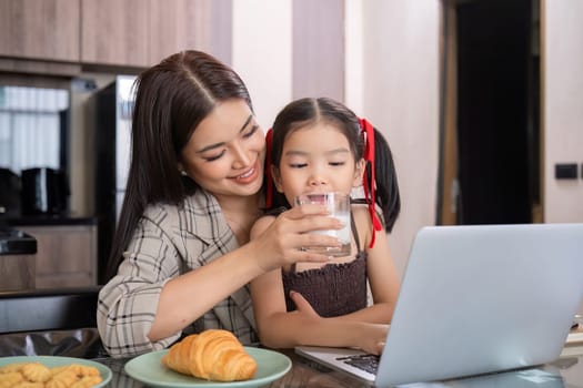 A young single mother receives a snack and eats it with her daughter while she works at home on her laptop..