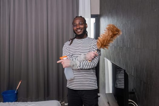 African man in casual clothes Clean dust or dirt in the room. Stand holding cleaning supplies and smile for the camera..