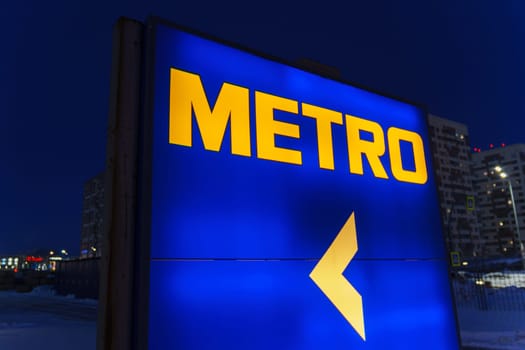 Tyumen, Russia-March 18, 2024: Metro sign glows brightly against the night sky, with the silhouettes of city buildings in the background.