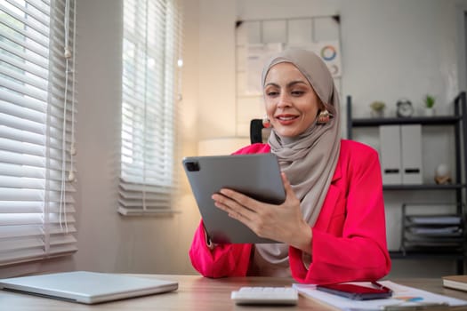 A female Muslim investor who trades in cryptocurrencies sits looking at stock charts and studying Bitcoin..