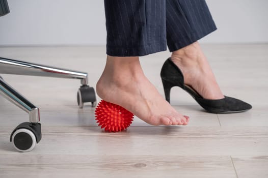 Business woman massages her feet on a massage ball with spikes