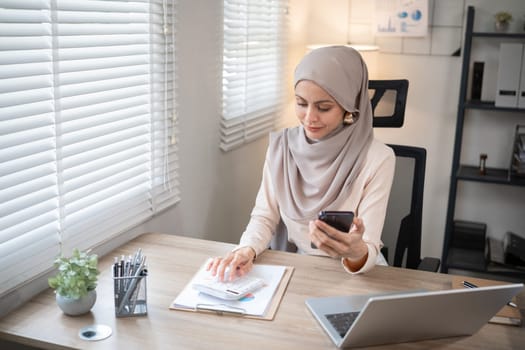 Muslim female entrepreneur wearing hijab sits working with laptop managing personal business in private office..