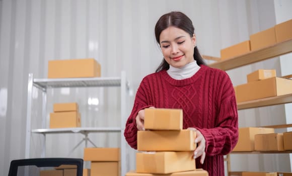 A female Asian online business entrepreneur prepares and packs merchandise into parcel boxes on a table to deliver to customers..