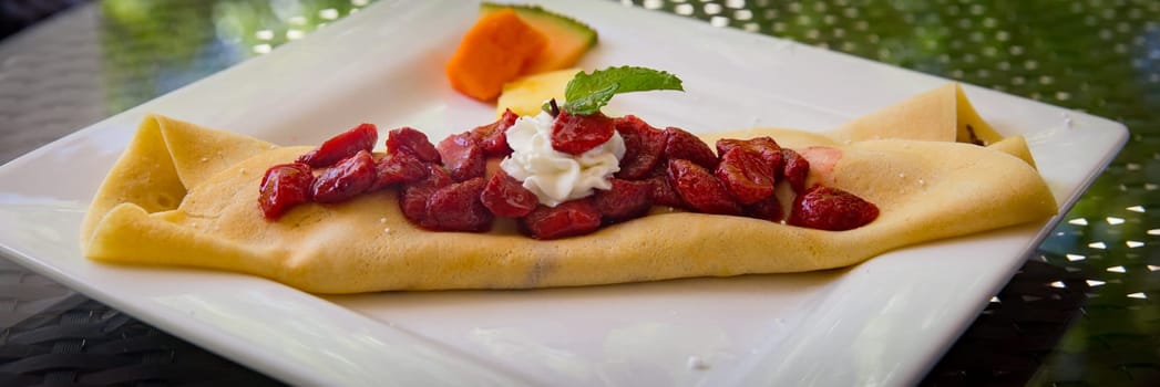 Strawberry Crepe garnished with Mint and some fruit on the side