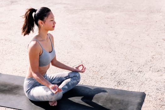 young asian woman in sportswear doing meditation on a yoga mat, concept of mental relaxation and healthy lifestyle, copy space for text
