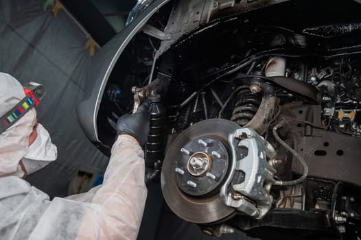 An auto mechanic applies anti-corrosion mastic to the underbody of a car