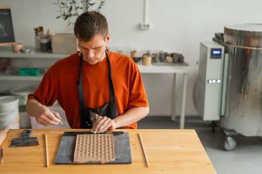 A potter cuts a piece of rolled clay with patterns