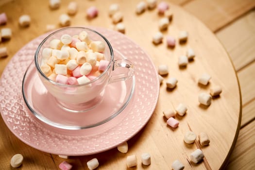 Cup with hot milk and colorful marshmallows on bright wooden table