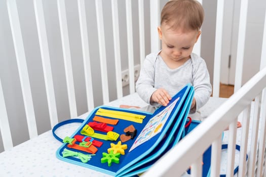 One year old baby sitting in a crib playing with montessori busy book