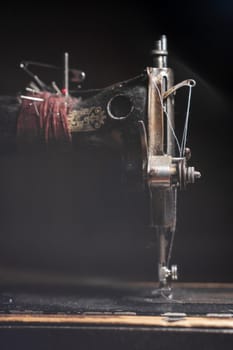 An old sewing machine stands on the table at home ready to work and sew. Classic retro style manual sewing machine ready for sewing work. The machine is old style made of metal with floral patterns