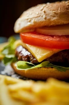 delicious cheeseburger surrounded by french fries on a black table