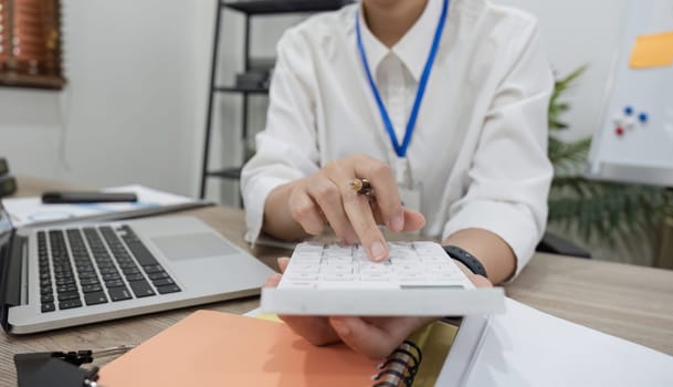 Asian female accountant Use a calculator to calculate business numbers on a white wooden table in the office..