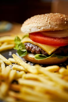 delicious cheeseburger surrounded by french fries on a black table