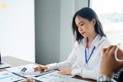 A man is talking to two women at a table with papers and a calculator. The man is wearing a watch and the women are wearing white shirts. The atmosphere seems to be professional