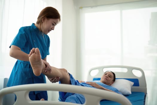 Physical therapist Asian woman, doing leg physiotherapy for elderly man to treat osteoarthritis and nerve pain in the leg to nursing at home and health care concept.