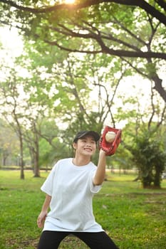 Shot of teenage Asian girl wearing leather glove playing baseball at public park.