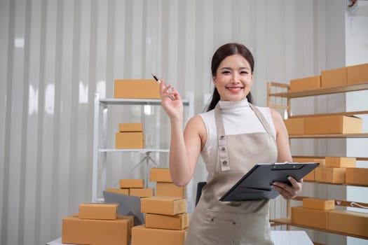 A small SME business owner writes inventory and shipping information on a clipboard in his home office. Small business operators preparing to ship to customers.