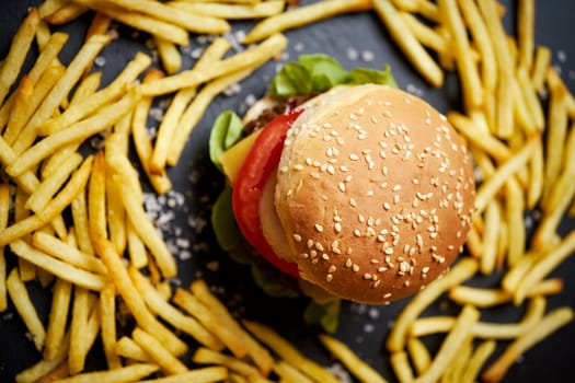 delicious cheeseburger surrounded by french fries on a black table