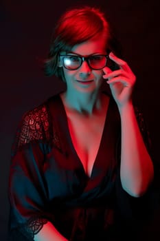 Beautiful attractive woman in glasses posing in satin bathrobe in neon light in the studio