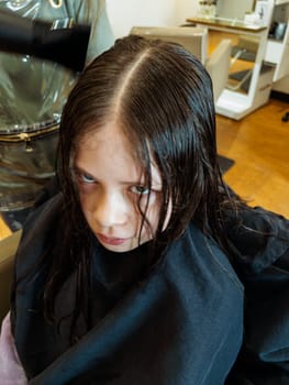 Gentle hands maneuver a hair dryer through a young girl's newly cut hair, showcasing the drying process after a meticulous trim. The warmth of the dryer breathes life into her locks, as they transform from damp to styled with care and expertise.