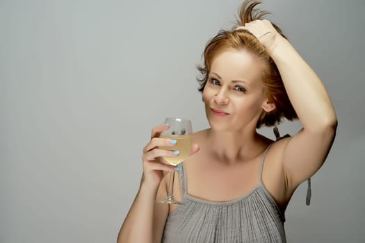 Portrait of young attractive beautiful red-haired woman with glass of white wine on gray background in studio