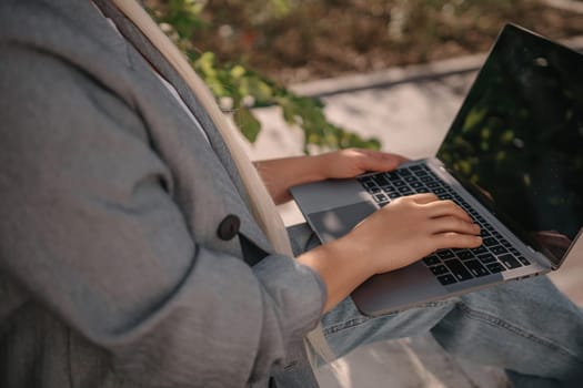 A person is sitting on a bench with a laptop open in front of them. They are typing on the keyboard, possibly working or browsing the internet. Concept of productivity and focus